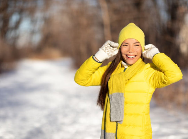 There's a woman in a yellow coat and beanie outside in the snow